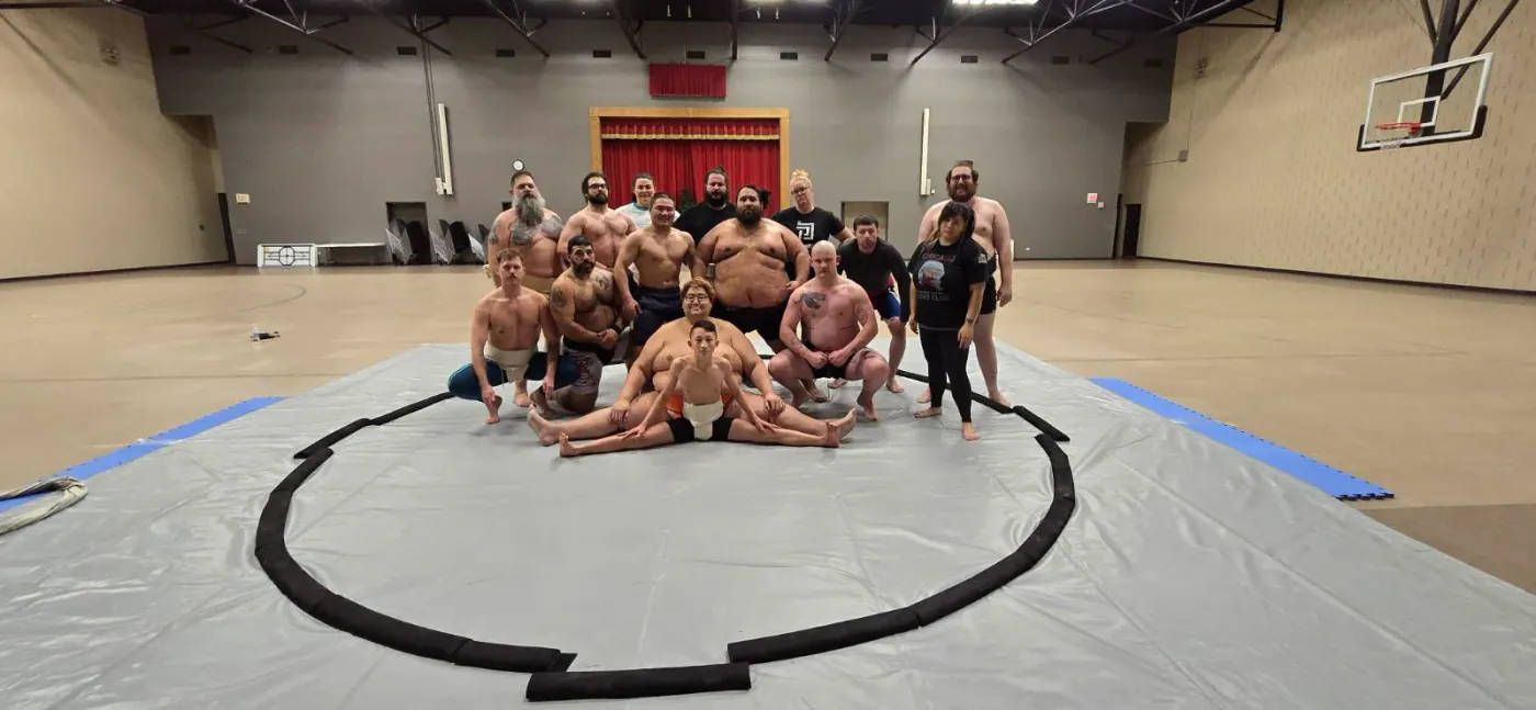 Club members arranged around the dohyo for a group photo in a gymnasium