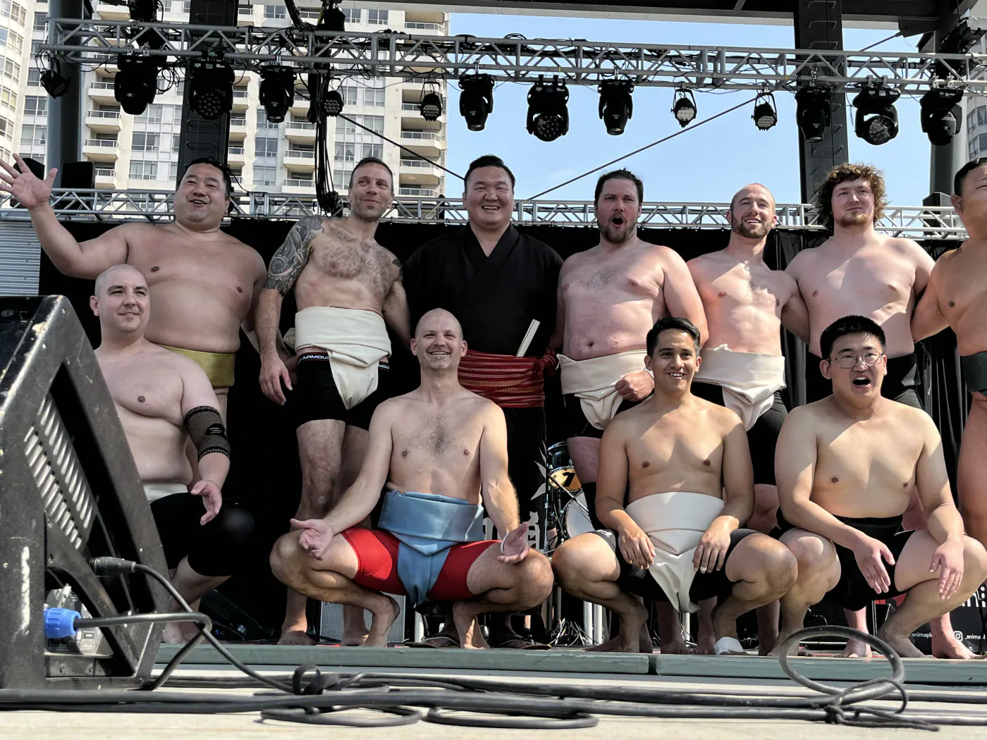 Wrestlers posing on an outdoor festival stage with a guest in a black kimono